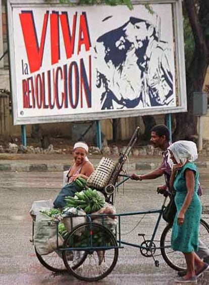 Tres cubanos pasan en La Habana ante un cartel conmemorativo del 40º aniversario de la revolución, en 1999.