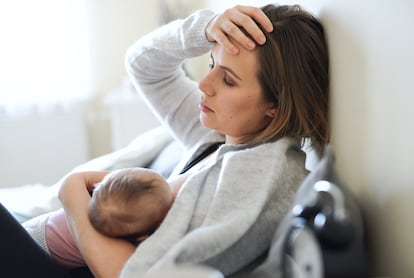 Tired mother nursing baby daughter indoors at home