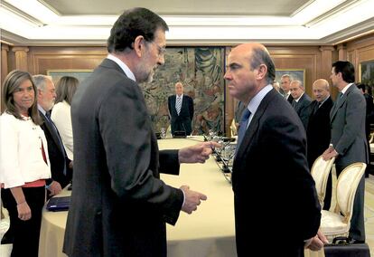 El presidente del Gobierno, Mariano Rajoy, conversa con el ministro de Economía y Competitividad, Luis de Guindos, al inicio de la reunión del Consejo de Ministros que presidió el rey Juan Carlos (al fondo) en el Palacio de la Zarzuela, el 13 de julio de 2012.