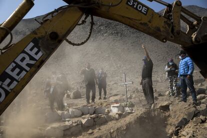 Unos familiares dan el último adiós a los restos de Juan Paucar Quispe mientras la retroexcavadora coloca su ataúd en la tumba asignada en el cementerio de Carabayllo. Durante el periodo de pandemia, el Sistema Nacional de Defunciones (Sinadef) ha llegado a registrar picos de casi 700 fallecidos a nivel nacional por cualquier causa, pero estos valores están descendiendo desde hace dos semanas en una lenta disminución a valores previos a la pandemia que eran de unos 200 fenecidos al día.