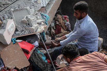 Una palestino intenta rescatar el cadáver de una persona atrapada entre los escombros de un edificio destruido tras un bombardeo israelí en Khan Yunis, este domingo.