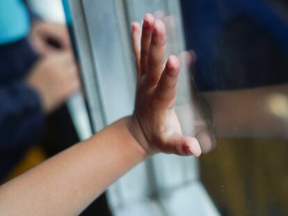 Un menor apoya su mano en una ventana, en una fotografía de archivo.