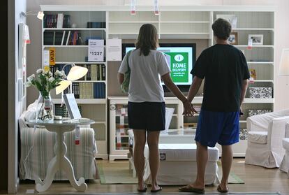 A couple holds hands in front of an empty living room at a Chicago IKEA.