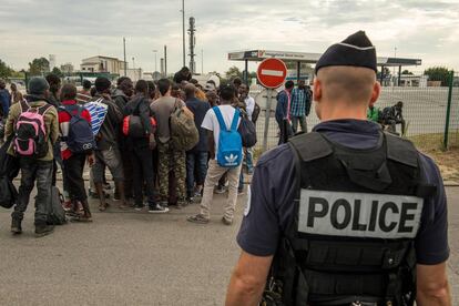 Un polic&iacute;a franc&eacute;s vigila a un grupo de migrantes reci&eacute;n llegado a la &#039;Jungla&#039; de Calais.