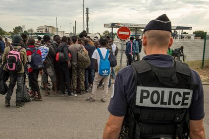 Un policía francés vigila a un grupo de migrantes recién llegado a la 'Jungla' de Calais.