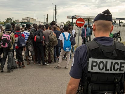 Un polic&iacute;a franc&eacute;s vigila a un grupo de migrantes reci&eacute;n llegado a la &#039;Jungla&#039; de Calais.