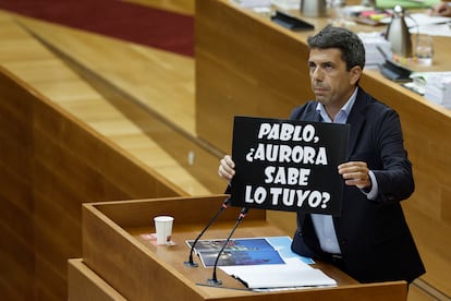 El president de la Generalitat, Carlos Mazón, muestra un cartel que alude al alcalde de Elche, Pablo Ruz, y a, su socia de gobierno Aurora Rodil, de Vox, durante su intervención en la sesión de control de las Cortes.