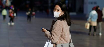 Una mujer con mascarilla camina por una zona comercial de Shanai.