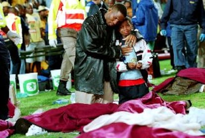 Un hombre y un niño, arrodillados sobre el césped, lloran junto a varios cadáveres.