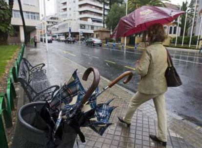 Una mujer pasa junto a una papelera llena de paraguas rotos por el viento, hoy en el centro de Huelva.