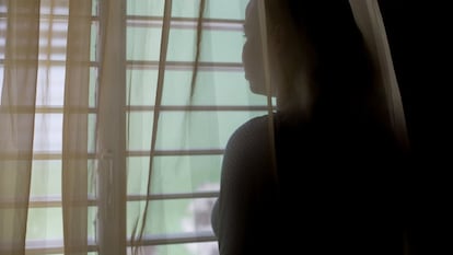 Una adolescente mira por la ventana sin dejar ver su rostro para proteger su identidad.