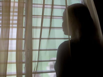 Una adolescente mira por la ventana sin dejar ver su rostro para proteger su identidad.