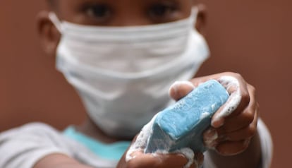 Un niño, con su mascarilla, sujeta un jabón para lavar sus manos.