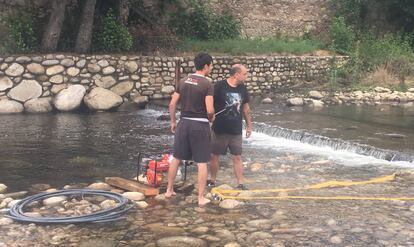 Javier Escudero, de espaldas, ayuda a recoger las cenizas del incendio en la piscina natural.