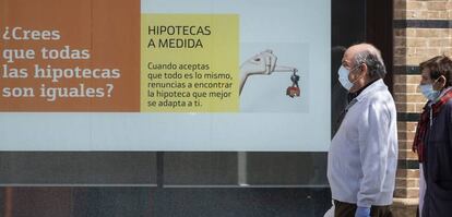 Dos personas pasan por delante de un cartel publicitario de un banco hoy en Sevilla.