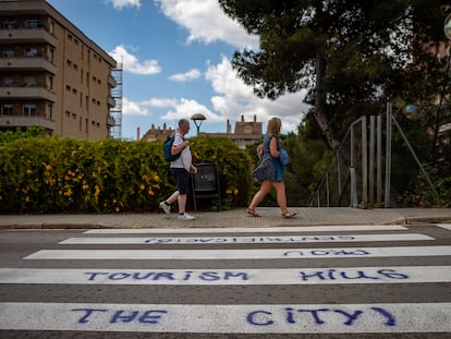 Un par de visitantes de Barcelona caminan ante una pintada en la calle en contra del turismo.