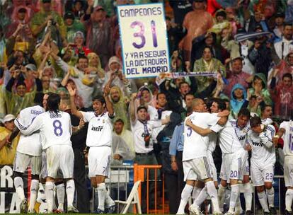 Los jugadores del Real Madrid celebran el tercer gol que le endosaron en el Bernabeu al Fútbol Club Barcelona, que como mandan los gestos de caballeros hizo el paeseillo al campeón. Un aficionado esgrime en una pancarta los 31 títulos de liga del equipo blanco, sin recordar que las dictaduras, además de malas, aburren por monótonas.