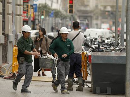 Dos trabajadores echan escombros en un contenedor en una calle de Barcelona.