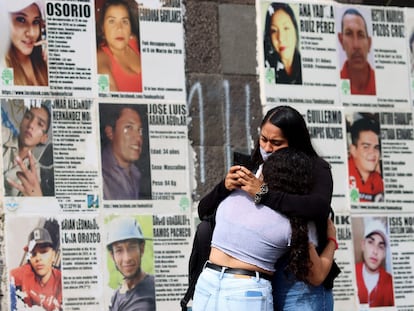 Dos mujeres se abrazan delante de imágenes de personas desaparecidas, en Guadalajara, Jalisco, este domingo.