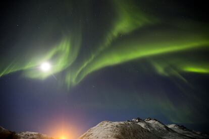 La aurora boreal envuelve la luna en la noche estrellada de Tromsø (Noruega).