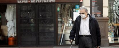 Una persona mayor protegida con mascarilla arrastra un carro frente a un comercio cerrado, en Valencia.