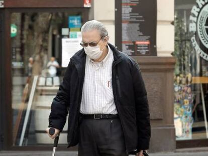Una persona mayor protegida con mascarilla arrastra un carro frente a un comercio cerrado, en Valencia.