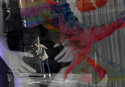 Un hombre limpia la calle bajo una bandera del orgullo en una calle del barrio madrileño de Chueca antes de la manifestación del Orgullo.