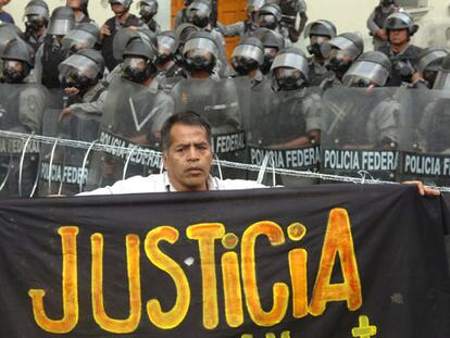 Un manifestante posa con una pancarta pidiendo justicia frente a los policías que bloquean una de las calles de acceso a la plaza principal de Oaxaca.
