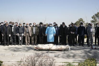 Un grupo de personas con mascarillas y guantes rezan ante el cuerpo del mando de la Guardia Revolucionaria Farzad Tazari, en el cementerio Behesht-e-Zahra, a las afueras de Teherán (Irán).