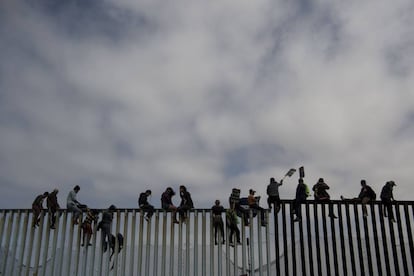 Gente sentada sobre la reja fronteriza en Tijuana, México.