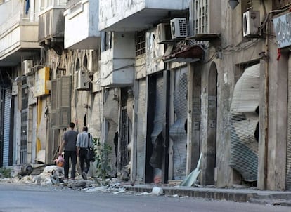 Unos habitantes de Homs pasan delante de tiendas dañadas por los enfrentamientos entre el régimen y los opositores, el 12 de julio de 2012.