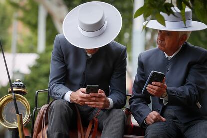 Dos cocheros manejan sus móviles, este miércoles en la Feria de Abril de Sevilla.
