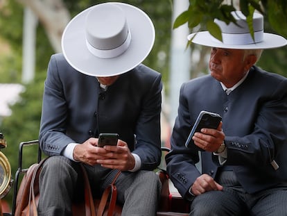 Dos cocheros manejan sus móviles, este miércoles en la Feria de Abril de Sevilla.