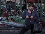 AME9937. SANTIAGO (CHILE), 14/05/2020.- Un habitante de calle duerme este jueves mientras una mujer con tapabocas carga sus compras en la Vega Central, principal mercado de abastos de Santiago (Chile). El Ministerio de Salud chileno informó este jueves que en las últimas 24 horas registraron el fallecimiento de 22 personas por coronavirus, la cifra más alta de decesos relacionados a la enfermedad desde su inicio en Chile el pasado 3 de marzo. EFE/Alberto Valdés