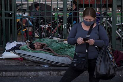 Una persona sin hogar duerme mientras una mujer carga sus compras en la Vega Central, principal mercado de abastos de Santiago (Chile).