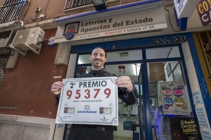 El gerente de la administración de loterías La Bruja Rockera, José María Imbernon, muestra el cartel del segundo premio del sorteo del Niño, en la calle Azucaque de Murcia.