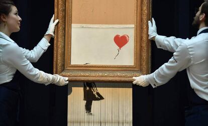 Empregados da Sotheby’s carregam a obra semidestruída de Banksy.