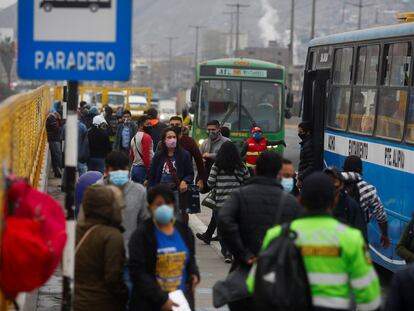 Varias personas pasan frente a una parada de autobuses en Lima (Perú).