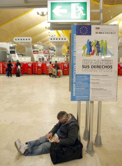 Un hombre espera su vuelo apoyado en un cartel que aboga por los derechos de los pasajeros.