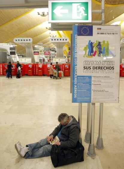 Un hombre espera su vuelo apoyado en un cartel que aboga por los derechos de los pasajeros.