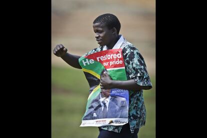 Un hombre porta un cartel de Nelson Mandela que reza 'Él restableció nuestro orgullo' mientras camina por una colina para obtener una buena vista del entierro.