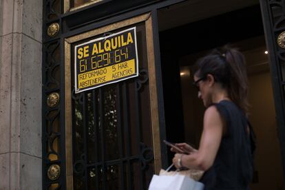 Una mujer pasa ante un portal en Madrid con un anuncio de un piso en alquiler, en julio.