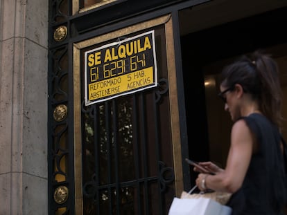 Una mujer pasa ante un portal en Madrid con un anuncio de un piso en alquiler, en julio.