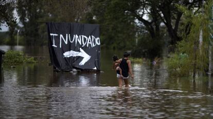 Mulher carrega bebê em área inundada na Argentina.