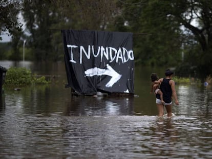 Mulher carrega bebê em área inundada na Argentina.