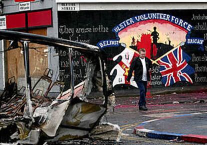 Un hombre pasa junto a un autobús que fue incendiado durante los disturbios registrados en Sandy Row.