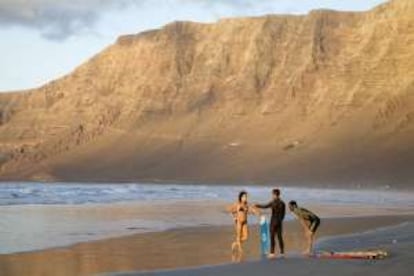 Riscos, surfistas y arena volcánica en la playa de Famara, en Lanzarote.