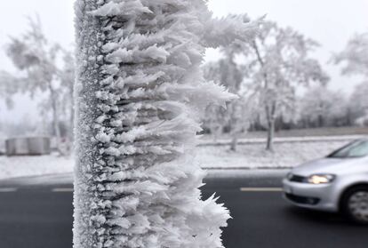 Un coche circula por una carretera rodeada de nieve en las montañas Hoher Meissnerm, Alemania. En primer plano el tronco de un árbol cubierto de carámbanos verticales muestra los efectos combinados del viento y las bajas temperaturas, el 2 de diciembre de 2014.