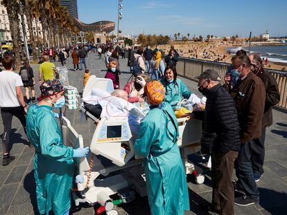 Un paciente con covid de 63 años, ingresado en el Hospital del Mar, sale al paseo marítimo acompañado por varios sanitarios en Barcelona.