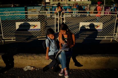 La venezolana Kimberly Gutiérrez ayuda a su hijo con la tarea en Cúcuta, Colombia, mientras esperan el bus escolar, en una fotografía de archivo. 